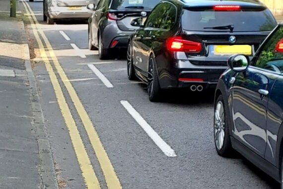 Existing cycling provision along London road is just a painted dotted white line making a narrow cycle lane. Some cars are driving in the cycle lane.